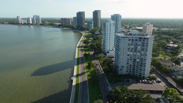 Drone shot of the sweeping curve of Bayshore Boulevard in Tampa, Florida, framed by modern condo towers, lush greenery, and the calm waters of Hillsborough Bay.