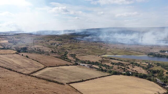 Aerial drone footage showing a wildfire spreading across a hillside in Wales, with flames, smoke and scorched vegetation visible across the landscape.