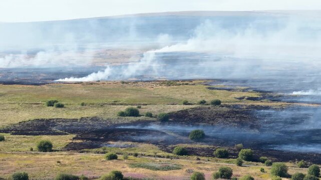 Aerial drone footage showing a wildfire spreading across a hillside in Wales, with flames, smoke and scorched vegetation visible across the landscape.