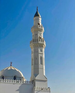 Low angle view of a white mosque minaret and dome with crescent finials against a clear blue sky.