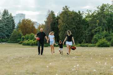 Fototapeta premium Cheerful family holding hands while walking through the summer park with a basket.