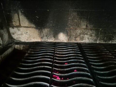 Close-up of cast iron grill grates over glowing red embers. Hot barbecue firebox ready for outdoor cooking