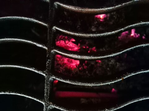 Macro view of glowing red embers through a cast iron grill grate. Intense heat and hot coals in a barbecue firebox