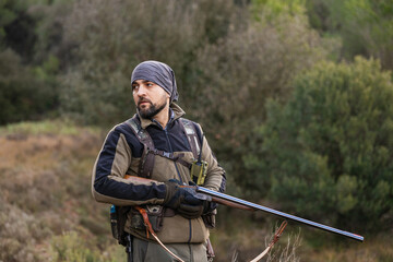 Fototapeta premium Hunter holding shotgun looking for game in forest