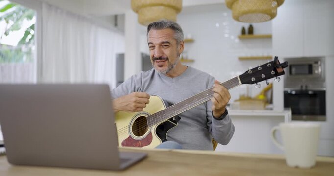 Portrait of elderly caucasian man musician as hobby. Senior male blogger teach guitar playing at living room. Handsome mature old man in casual clothes is smiling while playing guitar at home.