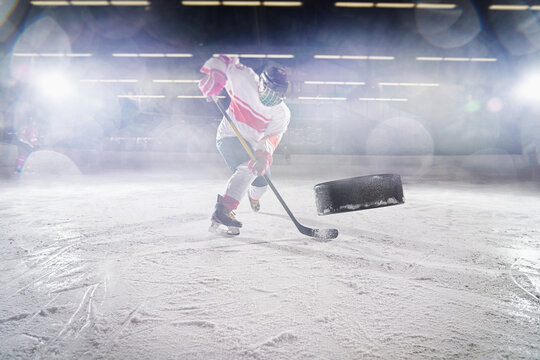 Ice hockey rink arena with professional player shooting the puck with hockey stick.