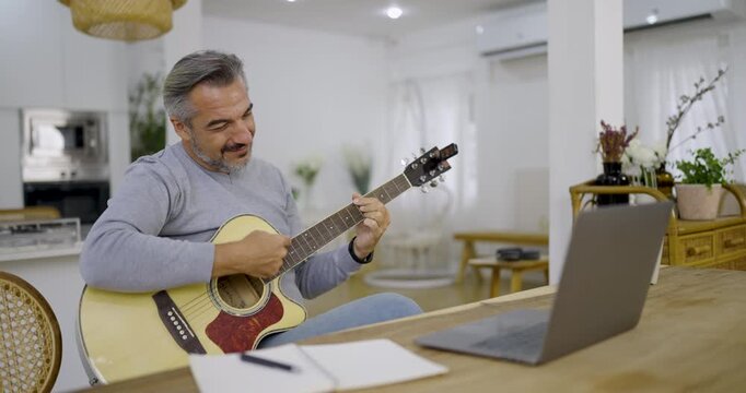 Portrait of elderly caucasian man musician as hobby. Senior male blogger teach guitar playing at living room. Handsome mature old man in casual clothes is smiling while playing guitar at home.