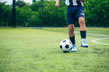 Obraz premium Kid boy leg kicking soccer ball on green grass field action. conceptual metaphor for youth sports training team competition fitness health wellness and active lifestyle 