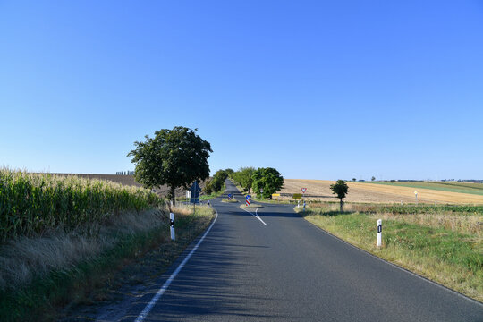 Gerade Landstra&szlig;e durch weite Felder unter blauem Himmel. L&auml;ndlicher Stra&szlig;enverkehr, Roadtrip, Sommerlandschaft, Landwirtschaft, Mobilit&auml;t und ruhige Fahrt durch die Natur.