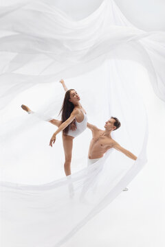 Poised ballerina balances high extension beside kneeling male dancer. Concept of discipline, flexibility, supportive partnership, personal growth, and artistic excellence.