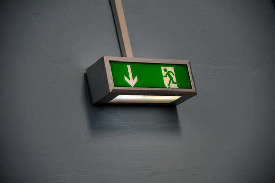 Gr&uuml;nes Notausgangs- und Fluchtwegschild mit Pfeil und laufender Person an einer Wand. Sicherheit, Evakuierung, Fluchtweg, Notausgang, Brandschutz und Geb&auml;udekennzeichnung.
