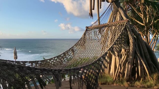 Rope Hammock Hanging on Exotic Tree Overlooking Ocean Coastline at Sunset
