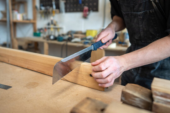 Skilled craftsman in restoration workshop sawing end of wooden board with hand saw instrument at workbench,, carpentry worker removing damaged wood with tool, preparing wooden piece for restoration.