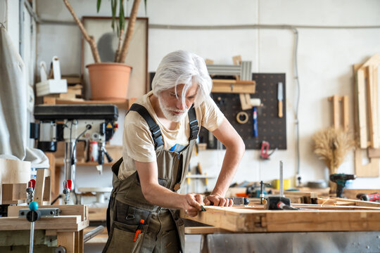 Pensive man restorer sanding surface of wooden door at workbench in restoration workshop, creative routine workflow in carpentry, craftsman polishing vintage object, perfecting and smoothing wood.