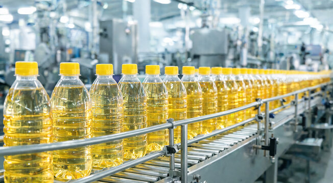 Production line shows plastic bottles filled with cooking oil in a factory setting during daytime