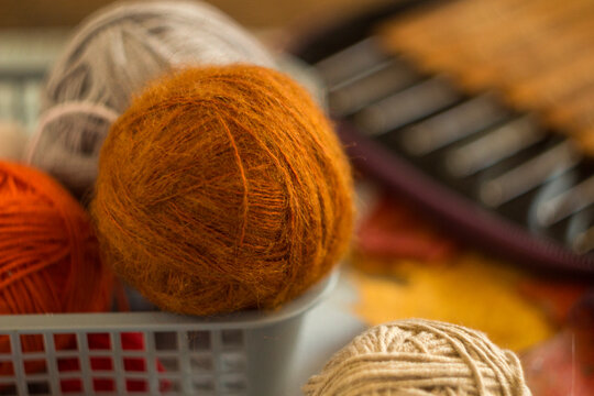 Cozy ball of fuzzy orange mohair wool yarn sitting in a basket. Close-up photo of soft knitting material for autumn handicraft, textile hobbies, and warm needlework concepts.