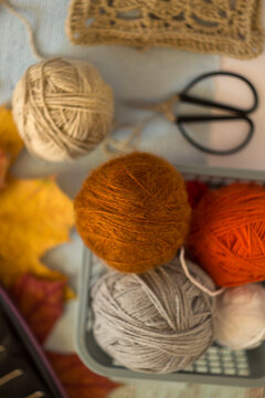 Cozy autumn flatlay with orange and gray wool yarn balls, vintage scissors, crochet lace, and fall leaves. Warm flat lay photograph for needlework and craft hobby concepts.