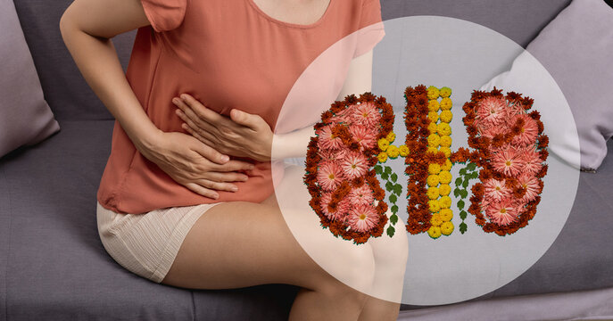 Woman sitting on a sofa holding her painful right flank next to a floral kidney composition. Kidney stones treatment, renal colic, and pyelonephritis diagnostics