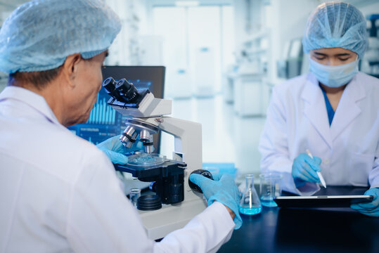 Two scientists collaborating in a modern biotechnology laboratory using laptop and microscope for biomedical research, healthcare innovation