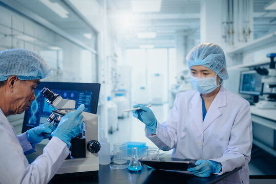 Two scientists collaborating in a modern biotechnology laboratory using laptop and microscope for biomedical research, healthcare innovation