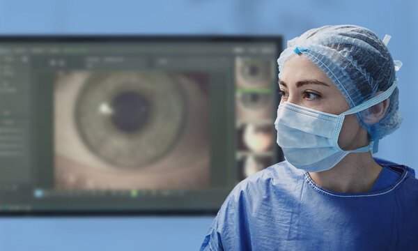 Female ophthalmic surgeon in protective mask and cap standing in front of a digital eye scan display. Cataract surgery treatment, glaucoma, and laser vision correction
