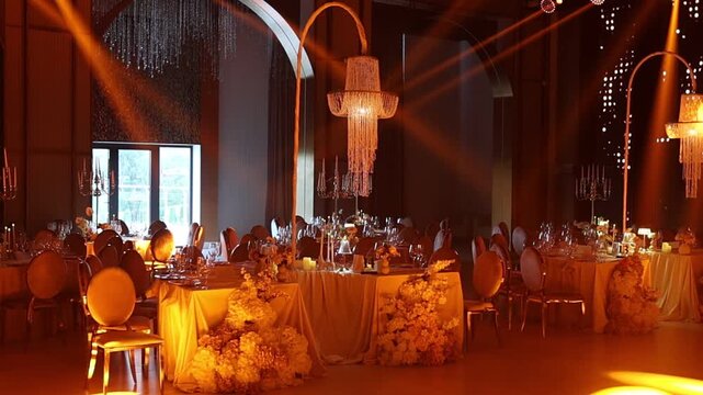 Warmly lit banquet hall with crystal chandeliers and moving amber spotlights over prepared head table, with banquet, chandelier, spotlight, uplight detail, showing table, centerpiece, floral, flower