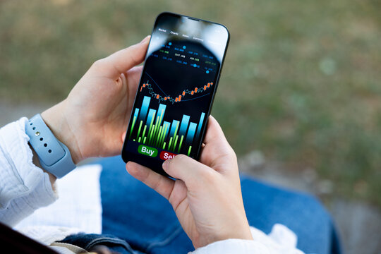 Woman behind a bench, holding a smart phone with stock maket information, chart and market data. Online trading, investment, stock prices, financial advisor, assets, wealth.