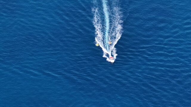 Aerial top down view of motorboat towing water tubes on deep blue sea during summer vacation in Corfu island Greece