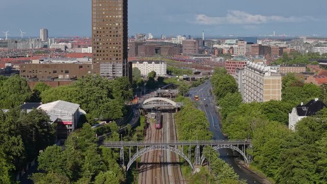 Aerial drone footage following a moving train through Copenhagen, showcasing the city's colorful architecture, railway infrastructure, rooftops, and dynamic urban environment.