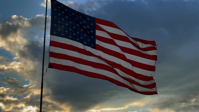 US flag waves gracefully with dramatic clouds and sunlight.