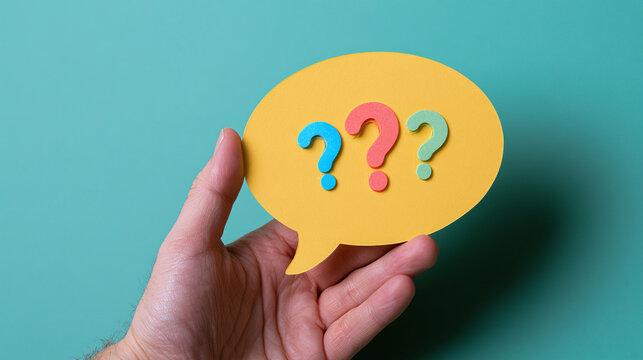 Hand holding yellow paper speech bubble with colorful question marks sign