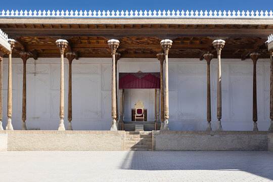 Throne room of the Ark Fortress in Bukhara with carved wooden columns and golden throne under a crimson canopy. Historic Uzbekistan landmark ideal for travel publications and cultural heritage.
