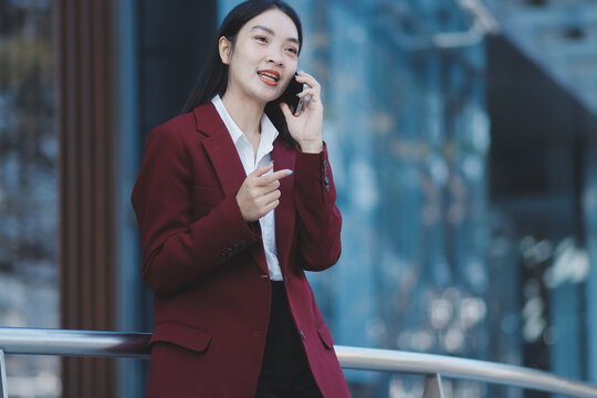 Young professional woman talking on phone and holding coffee outside modern office building