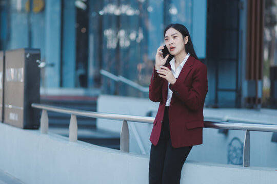 Young professional woman talking on phone and holding coffee outside modern office building