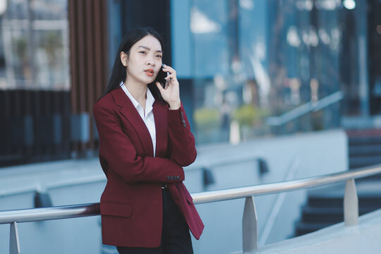 Young professional woman talking on phone and holding coffee outside modern office building