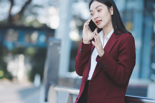 Young professional woman talking on phone and holding coffee outside modern office building
