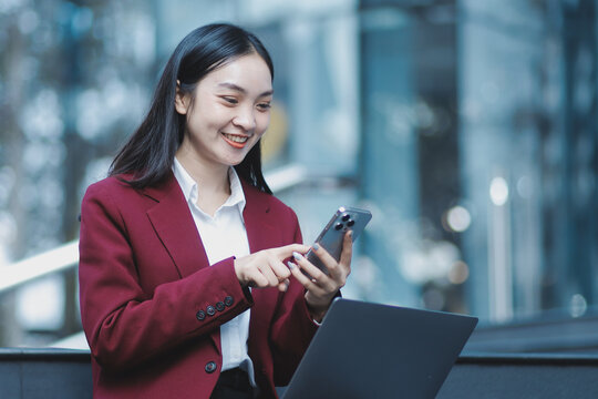 Focused woman in blazer types on laptop outdoors. Urban professional works remotely on stairs. She uses modern tech for business and connection.
