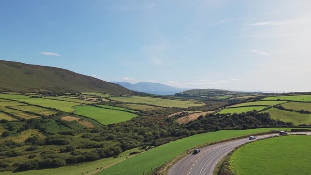 A wide aerial shot capturing the lush green hills, stonewalled fields, and winding coastal roads of Dingle, Ireland. Ideal for travel documentaries and sustainability themes.
