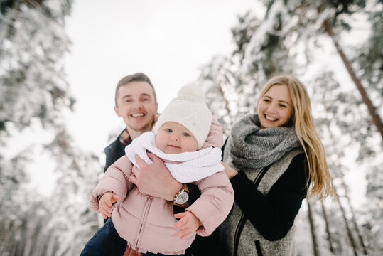 Happy parents holding their smiling little daughter during a winter walk in a snowy forest. Family joy, mom and dad spending time with a child in winter. Closeup.