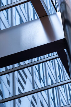 Dark steel beams cross a glass roof in an abstract architecture detail where geometric reflections form layered structural patterns across the frame