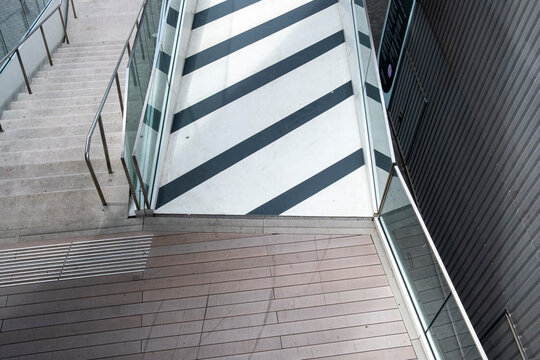 Geometric stairs and walkway beside a glass facade create striped shadows and strong lines in a contemporary architecture detail viewed from above