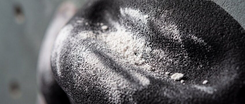 Black textured climbing hold with white chalk powder deposit offers reliable grip and friction for indoor rock climbing practice