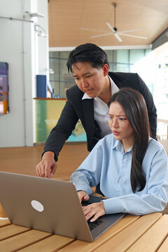 Asian Business Colleagues Collaborating on Laptop in Modern Outdoor Workspace