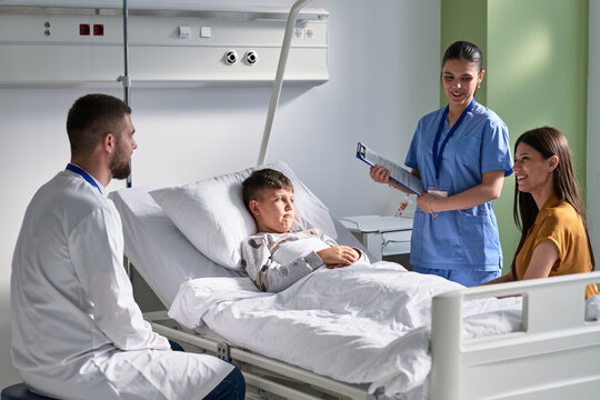 Healthcare professionals discuss treatment plans with child patient in hospital room during daytime