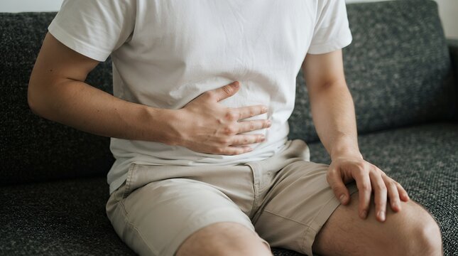 Stomach ache and abdominal pain, man holding belly with digestive issues, male patient suffering from cramps on sofa
