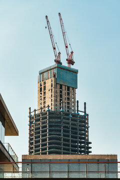 Skyscraper construction site with steel frame structure and tower cranes against blue sky