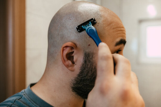 Close up of a young man shaving his head with a razor in a bathroom. Head shaving with a razor. A man shaving his head.