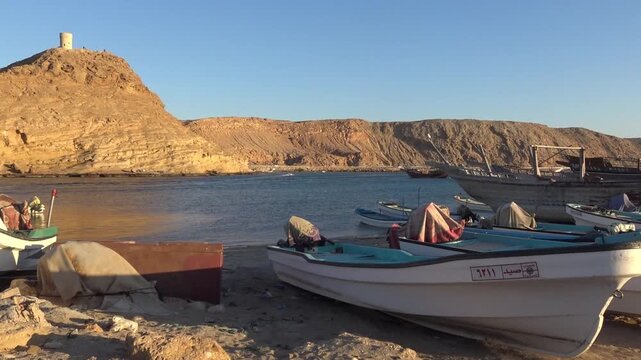 Fishing boats on the shore with a historic watchtower overlooking the bay, Sur, Oman