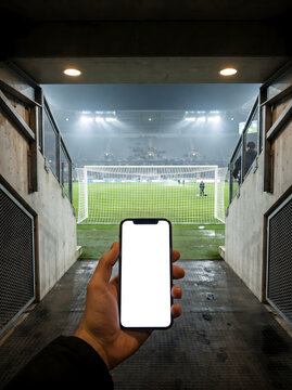 Hand holding a smartphone with a blank white screen inside a football stadium tunnel.