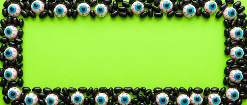 Creepy horror eyeball frame with black beans on neon green background for halloween party invitation flat lay top view photography style